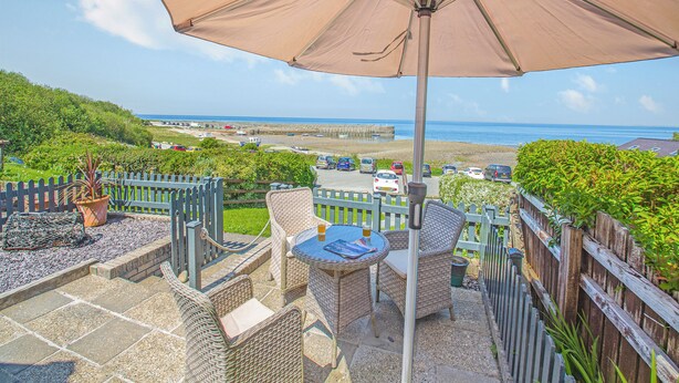 A patio with wicker furniture, a table, and an umbrella overlooking a beach.