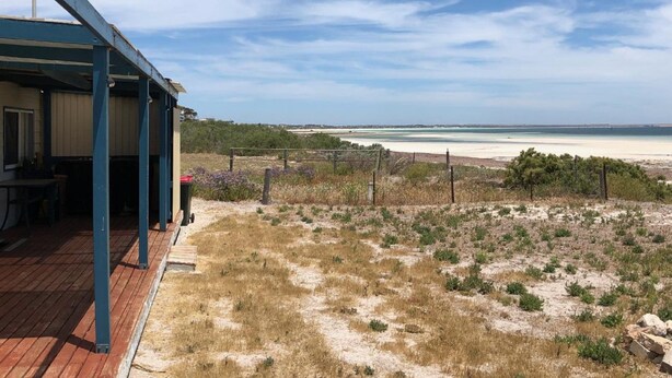 Ein Küstenanwesen mit überdachter Terrasse, Blick auf den Strand und spärlicher Vegetation.