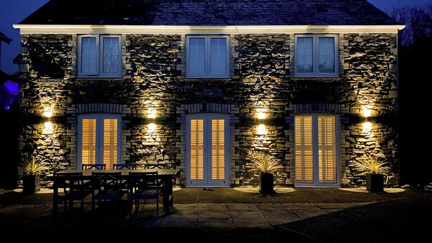 A stone building with a sign reading 'Barn Cottage' at the entrance, a covered patio area with outdoor seating, and a well-lit facade. - 3 bedroom accommodation in St Mawgan (St Mawgan)
