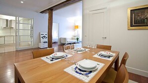 Une salle à manger avec une table en bois dressée pour quatre personnes, des murs blancs et une porte donnant sur une autre pièce.