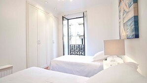 Une chambre d’hôtel avec deux lits, une table de chevet, une lampe, une armoire et une vue sur l’extérieur.