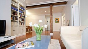 Un salon avec un téléviseur, des étagères à livres, une table basse avec un magazine et un canapé blanc.