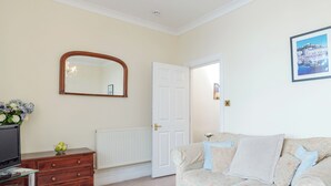 Een kamer met een houten dressoir, een witte radiator, een beige bank met opvallende kussens, een spiegel en een lijst met een afbeelding aan de muur.