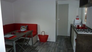 A compact living space with a kitchenette, a dining area with a red sofa and table, and a small red bag.