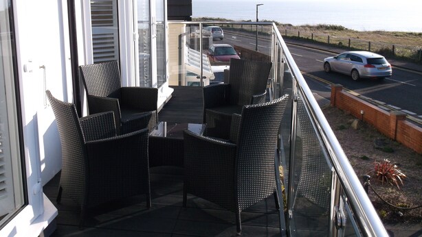 Een balkon met rieten meubilair, uitzicht op de weg en een gebouw met luiken.