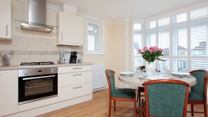 Een moderne keuken met witte kasten, een roestvrijstalen afzuigkap en een eetgedeelte met een ronde tafel en groene bekleden stoelen.