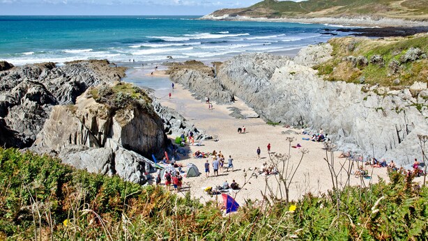 Una playa costera con terreno rocoso y gente practicando diversas actividades.