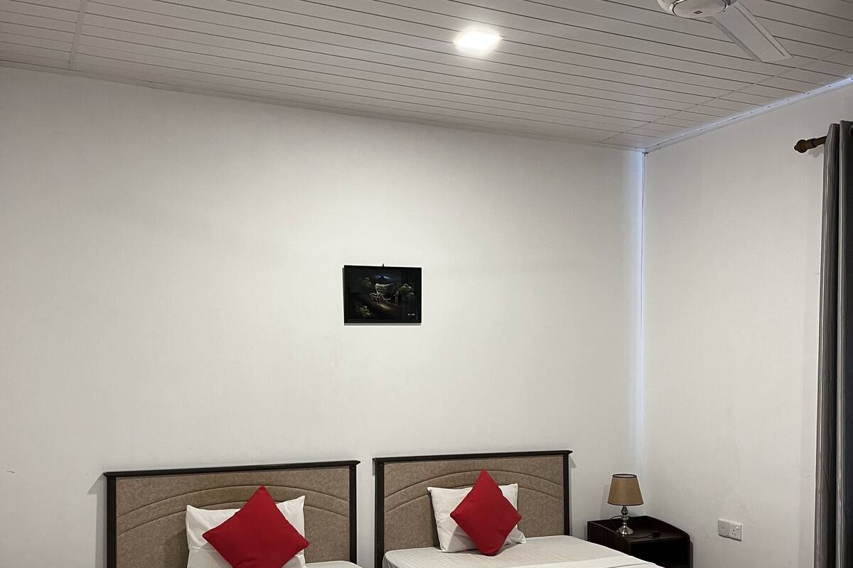 A room with two beds, a ceiling fan, a small table with a lamp, and a framed picture on the wall.