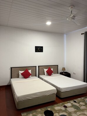 A room with two beds, a ceiling fan, a small table with a lamp, and a framed picture on the wall. - Siloonaa Garden Villa (Wariyapola)