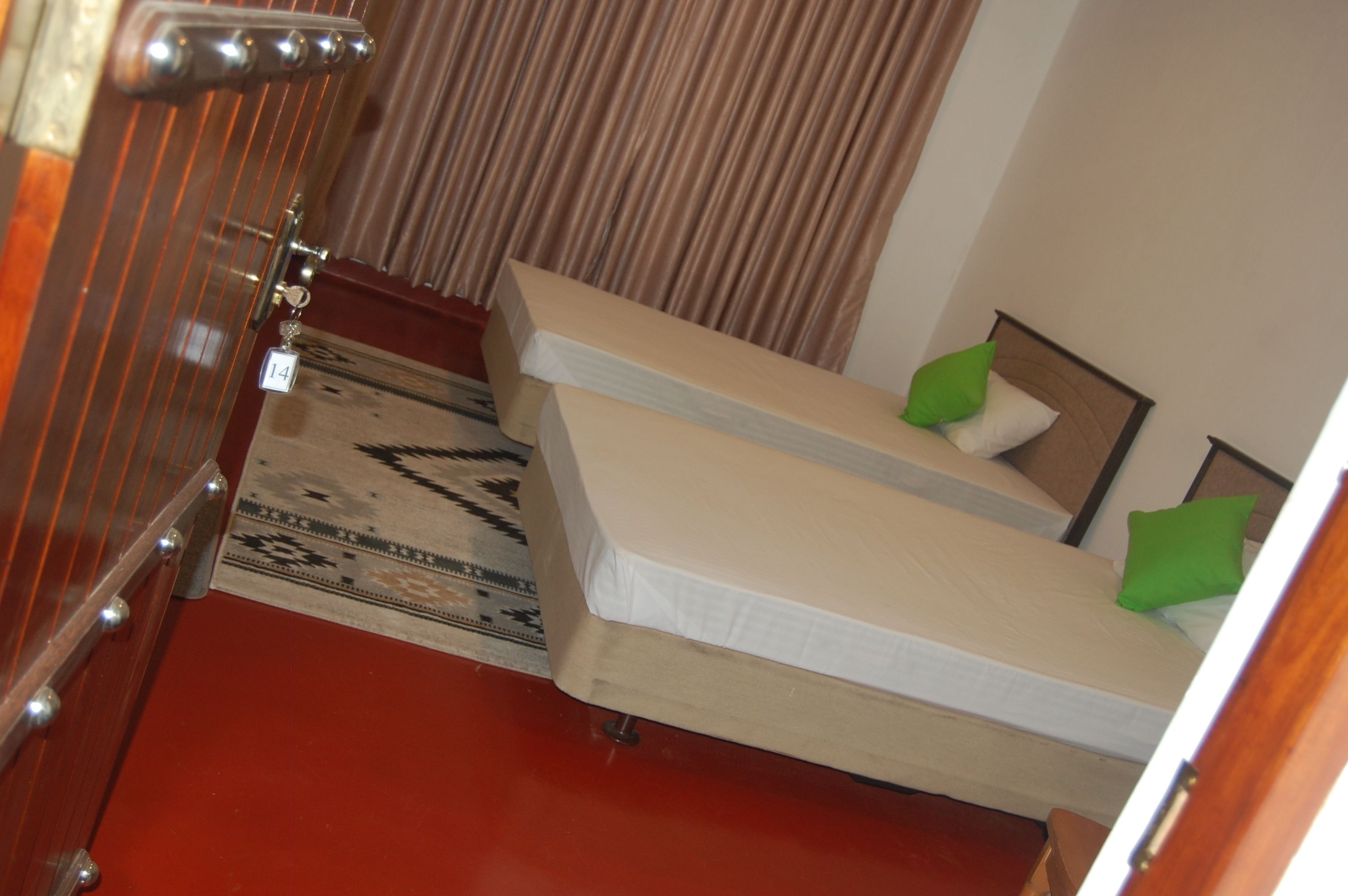 A room with two beds, a patterned rug, a wooden door, and a curtain.