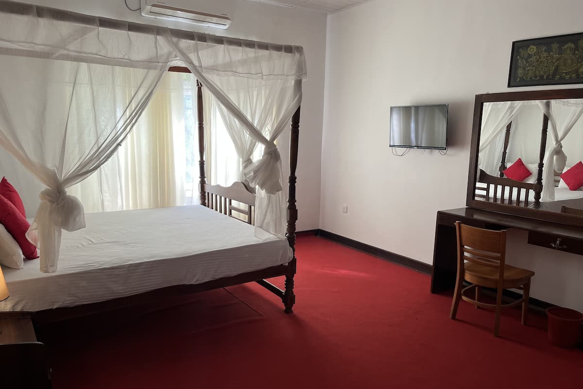 A room with a four-poster bed, a desk with a chair, a TV, and a mirror.