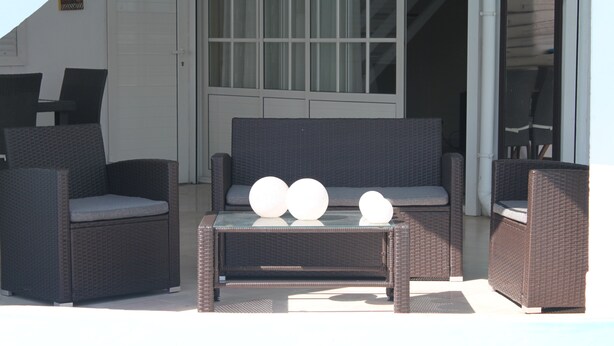 A patio area with wicker furniture, including a sofa and chairs, and a small table with decorative balls. - Bed and Breakfast in villa LAURAYM (Baie Mahault)