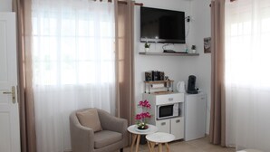 A modern living room with a sofa, a small round table, a TV mounted on the wall, a microwave, and a coffee maker. - Bed and Breakfast in villa LAURAYM (Baie Mahault)