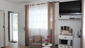 A modern living room with a flat-screen TV, a comfortable armchair, a small table with a vase of flowers, a microwave, and a coffee maker. - Bed and Breakfast in villa LAURAYM (Baie Mahault)