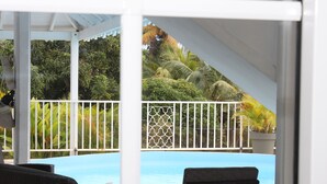 A covered outdoor area with a pool, wicker furniture, and a white fence. - Bed and Breakfast in villa LAURAYM (Baie Mahault)