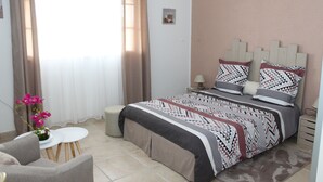 A bedroom with a bed, a small table, a chair, and a window with curtains. - Bed and Breakfast in villa LAURAYM (Baie Mahault)