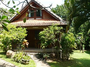 A wooden house with a tiled roof, surrounded by lush greenery and a stone pathway leading to the entrance. - Le Jardin (Karangasem)