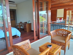 A room with a bed, a desk, a chair, and a balcony with wooden furniture. - Le Jardin (Karangasem)