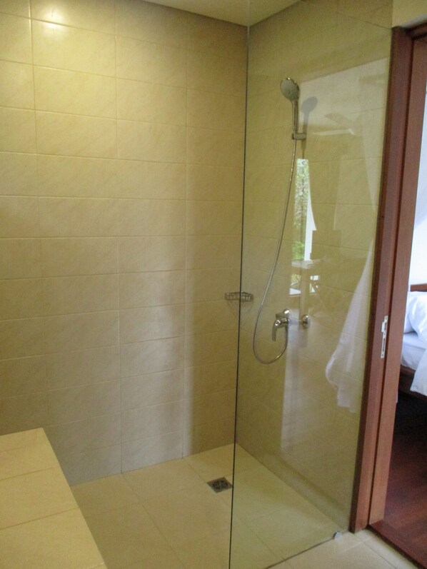 Zona de ducha con paredes de azulejos y ducha a la vista, protegida por una mampara de vidrio.