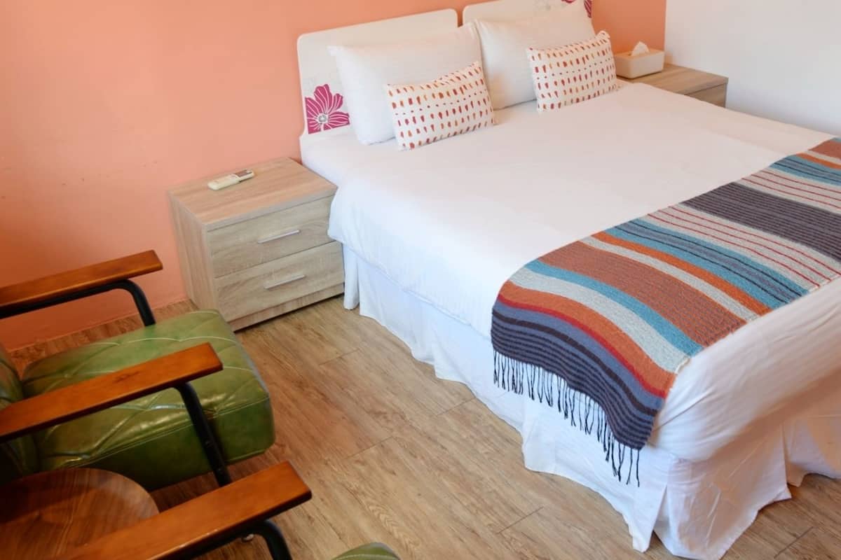 A bedroom with a bed, a nightstand, a chair, and a painting on the wall.