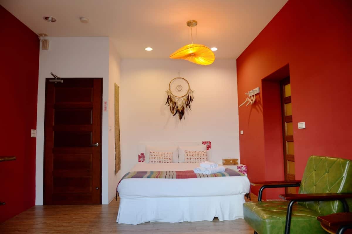 A bedroom with a bed, a dreamcatcher, a green chair, and a red wall.