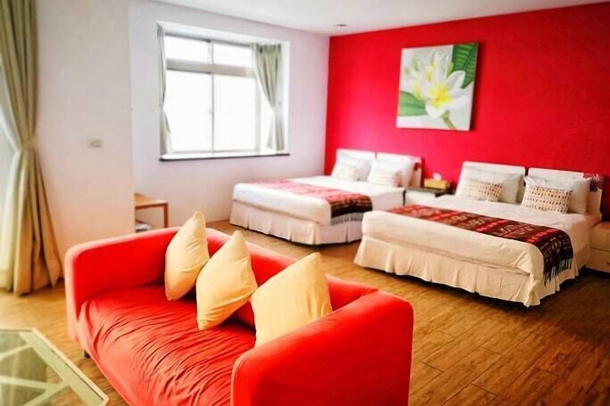 A hotel room with a red sofa, two beds, a window with curtains, and a painting on the wall.