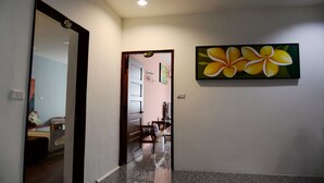 A hallway with a mirror, a painting of yellow flowers, and a door leading to a room with a bed and a dresser. - Rusty inn (Hengchun)