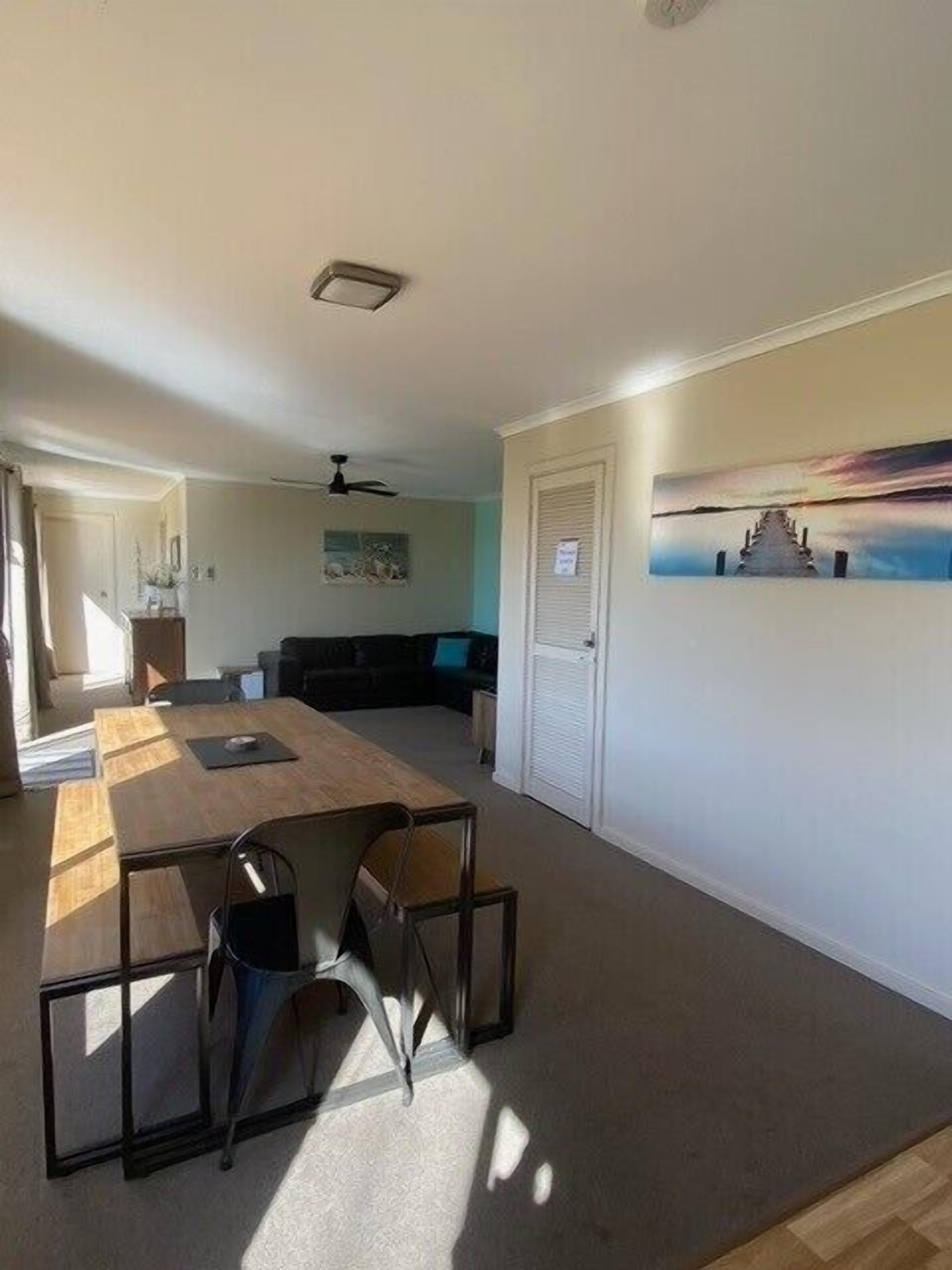 A room with a wooden dining table, chairs, a black sofa, a painting, and a door with a sign.