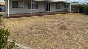 Ein Bungalow mit überdachter Veranda, kleinem Garten und bewölktem Himmel.