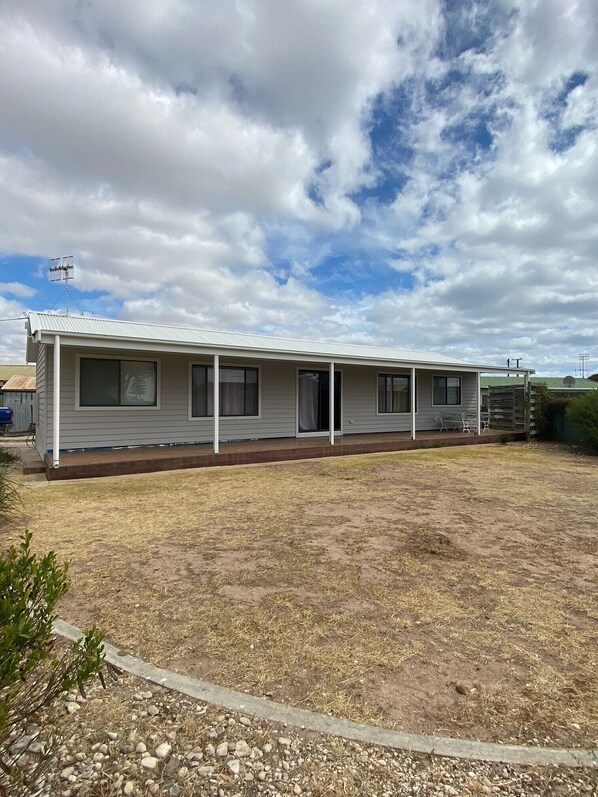 A single-story mobile home with a covered porch, a small yard, and a cloudy sky.