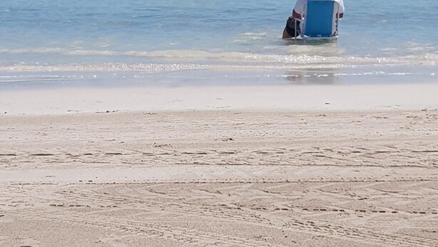 Eine Person sitzt auf einem Liegestuhl und blickt aufs Meer.