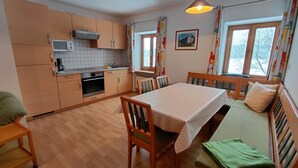 Ett kompakt kök med träskåp, ett matbord med stolar, en bänk och ett fönster med gardiner.