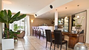Ein moderner Essbereich mit langem Tisch, Stühlen und einer Bar. Auf dem Boden befinden sich Kübelpflanzen und eine dekorative Metallkugel.