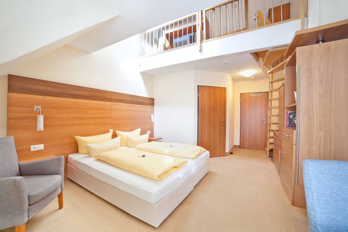 Ein modernes Schlafzimmer mit einem großen Bett, einem grauen Sessel, einem Holzkopfende und einem Einbauschrank.