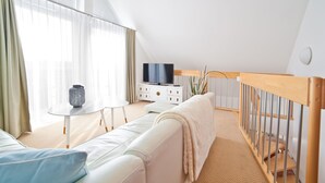 Ein modernes Wohnzimmer mit einem weißen Sofa, einem kleinen runden Tisch und einem Fernseher auf einem weißen Schrank.