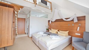 Ein modernes Schlafzimmer mit Schlafplatz in Podesteinlage, einem Holzkopfende und einem grauen Sessel.