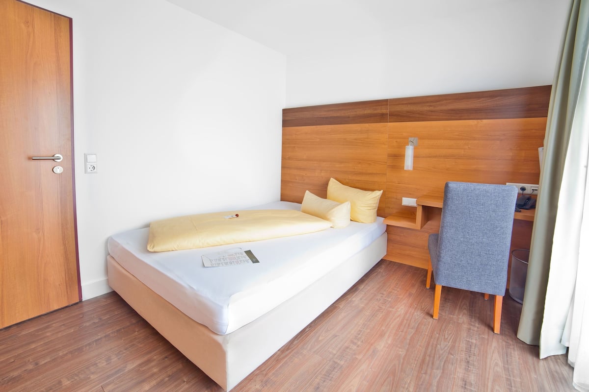 Ein Einzelbett mit Holz Kopfteil, einem Nachttisch und einem Stuhl.