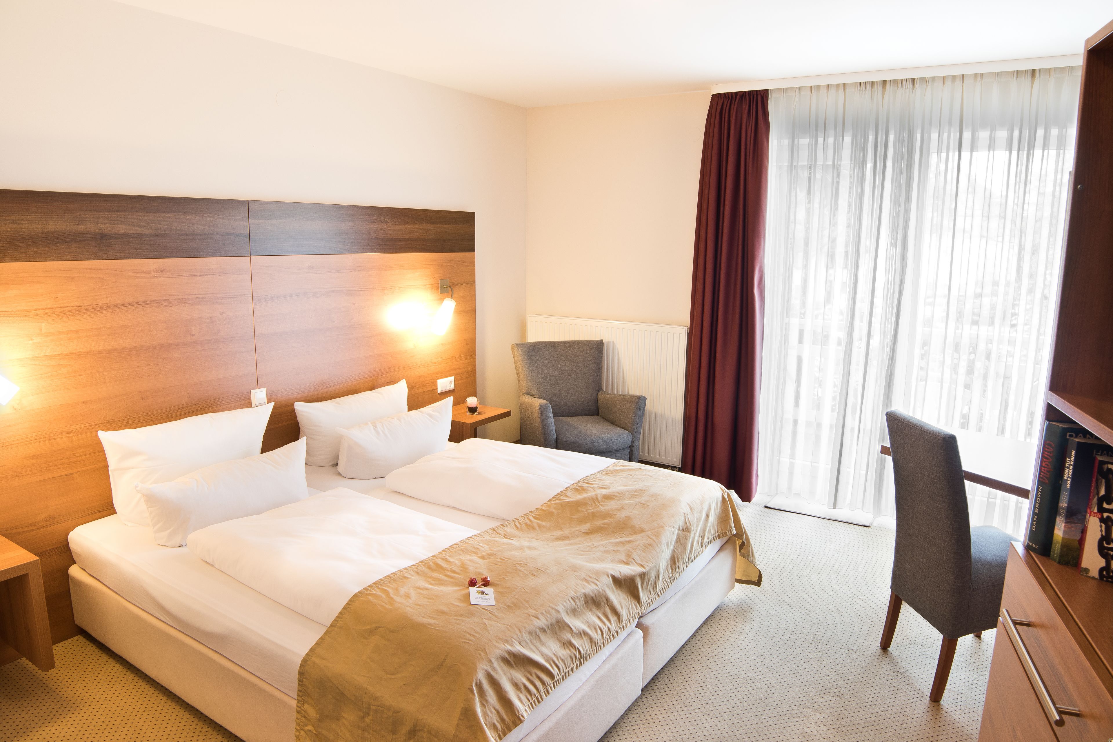 A hotel room with a large bed, a desk, a chair, and a window with curtains.