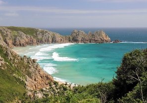 A coastal landscape with rocky cliffs, turquoise waters, and a beach.