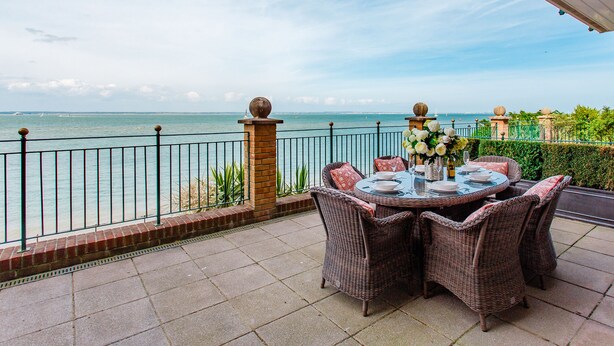 A terrace with wicker furniture, a table set for dining, and a view of the sea.