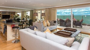 A spacious living area with a sofa, dining table, and chairs, a kitchen area, and a balcony with a view of the sea.