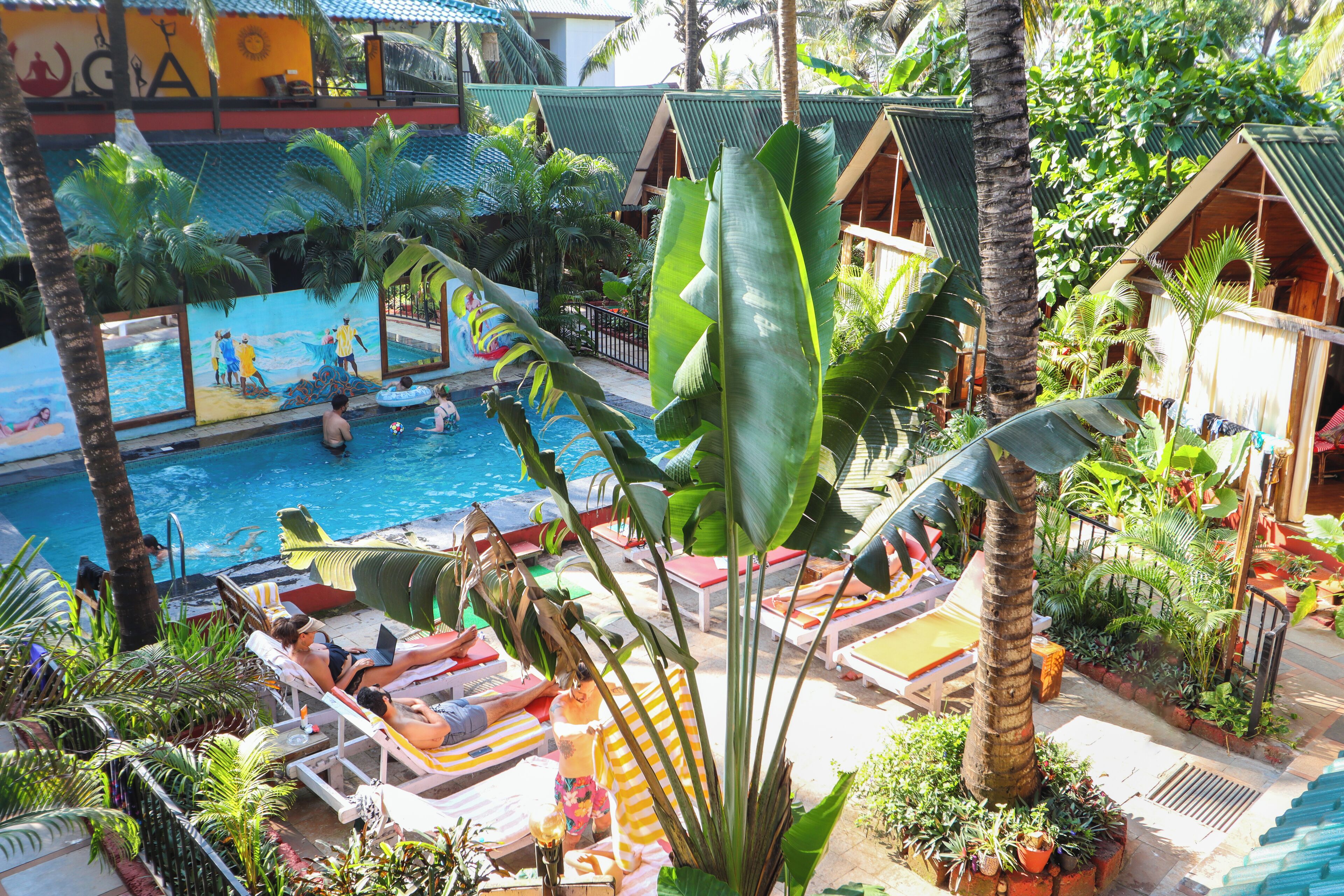 A pool area with lounge chairs and umbrellas, surrounded by tropical plants and wooden structures.