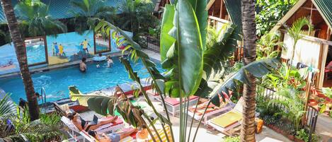 A pool area with lounge chairs and umbrellas, surrounded by tropical plants and wooden structures.
