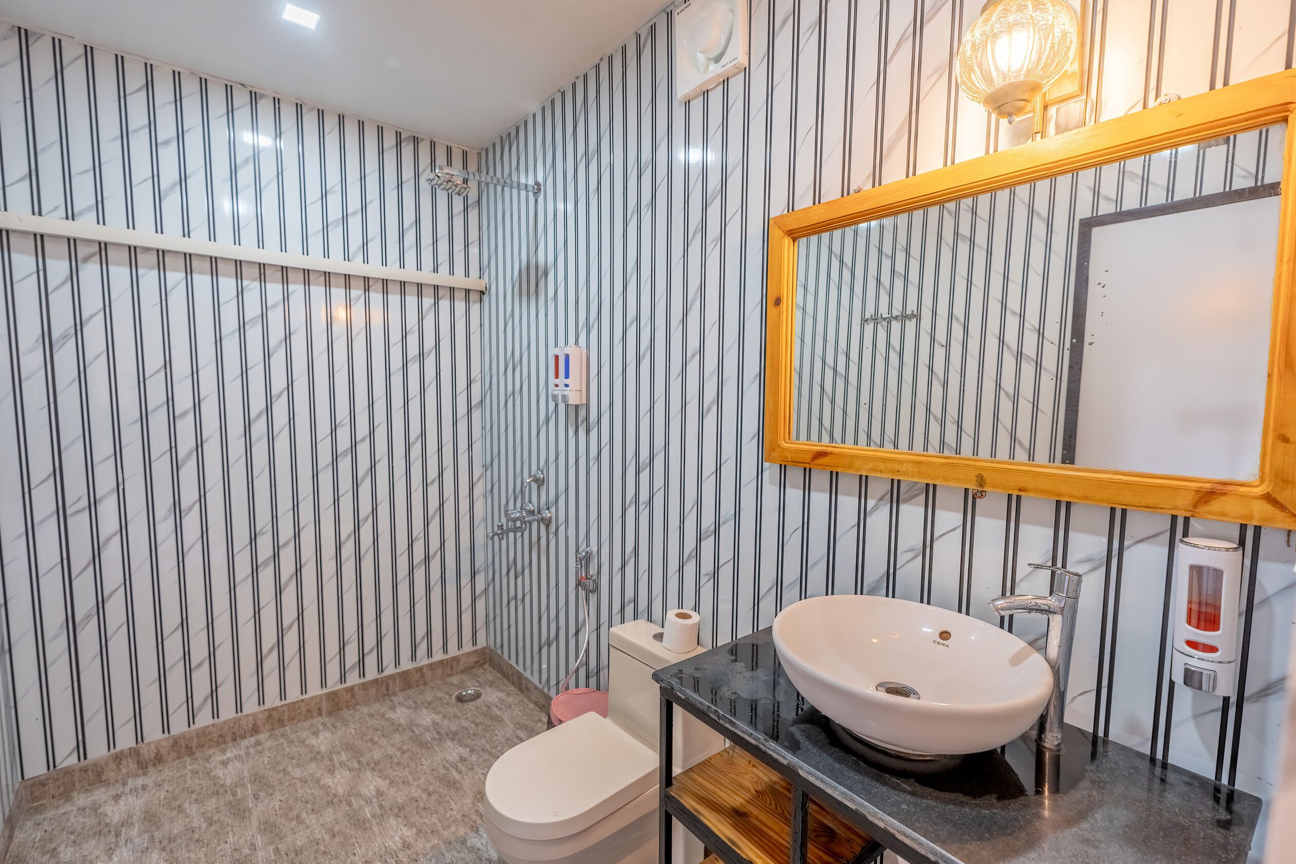 A bathroom with a marble-patterned wall, a white toilet, a sink with a wooden shelf, and a mirror with a wooden frame.