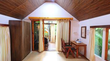 A room with wooden flooring, a wooden ceiling, a desk with chairs, and a view through a glass door to an outdoor area.