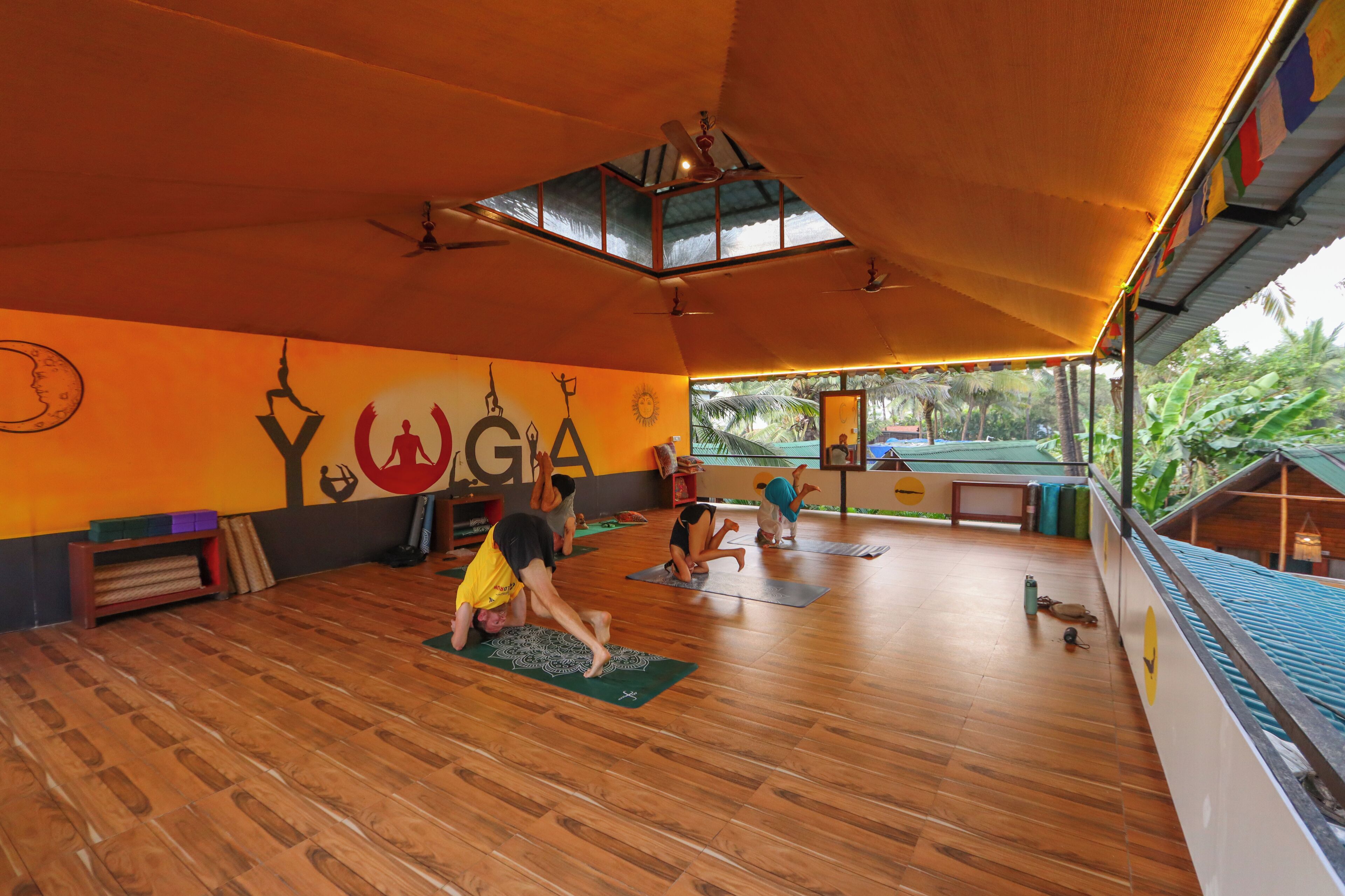 A yoga studio with wooden flooring, a sloped ceiling, and a large window overlooking a garden.