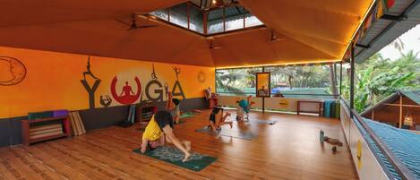 A yoga studio with wooden flooring, a sloped ceiling, and a large window overlooking a garden.