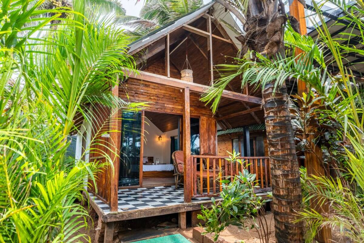 Uma cabana de madeira com deck xadrez, rodeada por vegetação tropical exuberante.