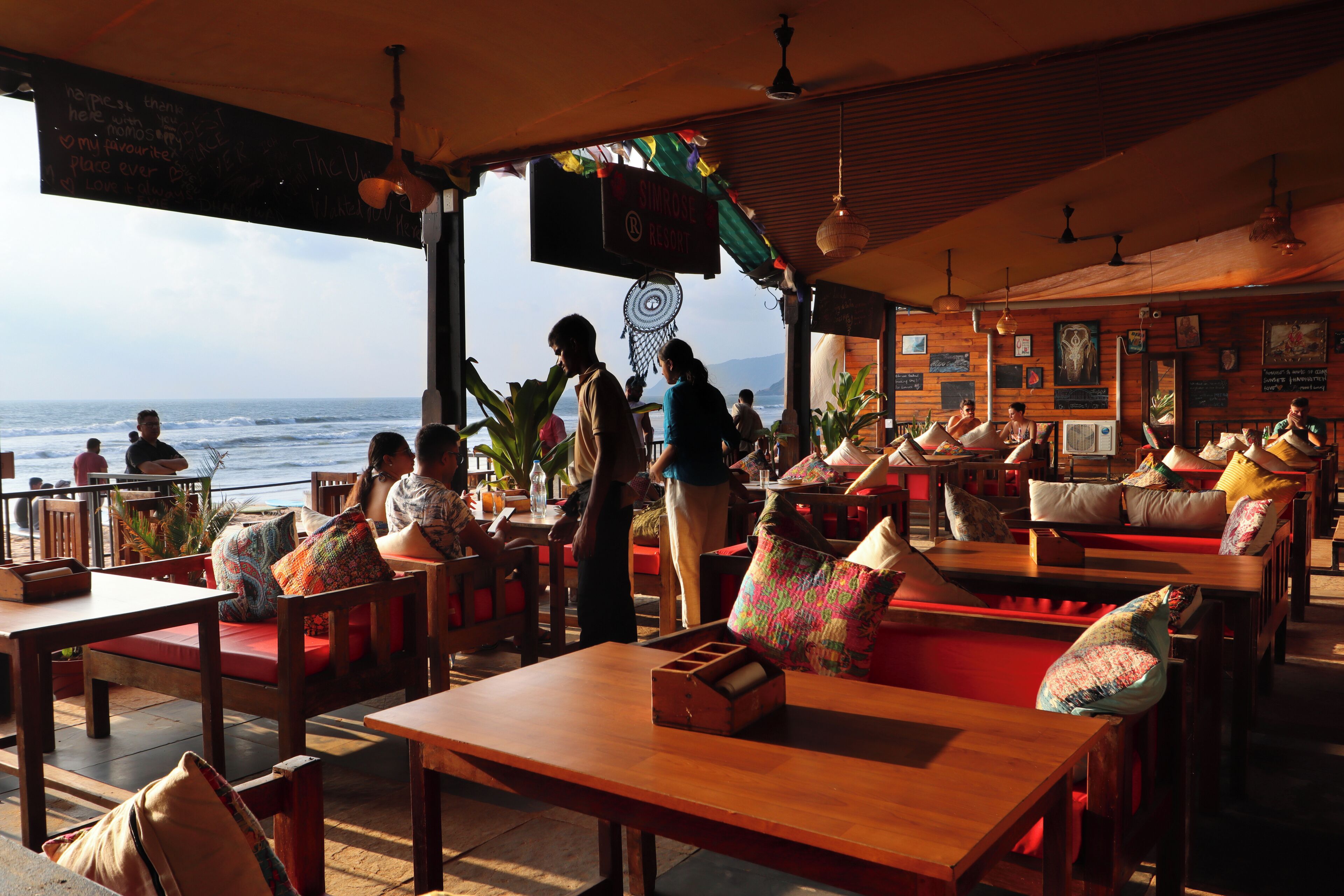 Een restaurant met houten meubels en uitzicht op de oceaan, met een bord waarop 'Singhose Resort' staat.
