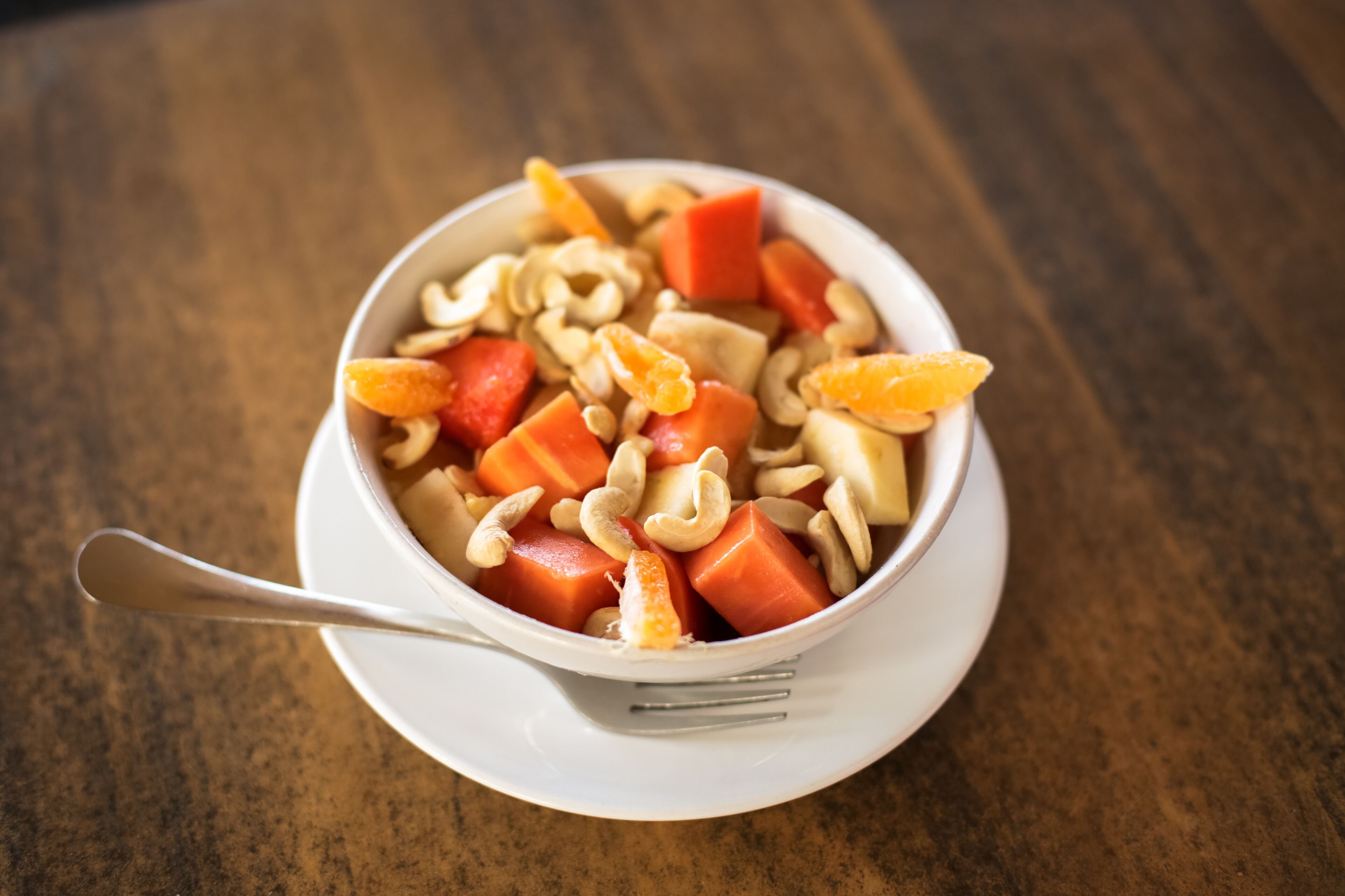 A bowl of fruit salad with nuts on a white plate.